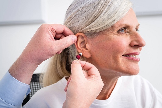 Ältere Frau bekommt ein modernes Hörgerät eingesetzt, Hörgeräte Anpassung Senioren.